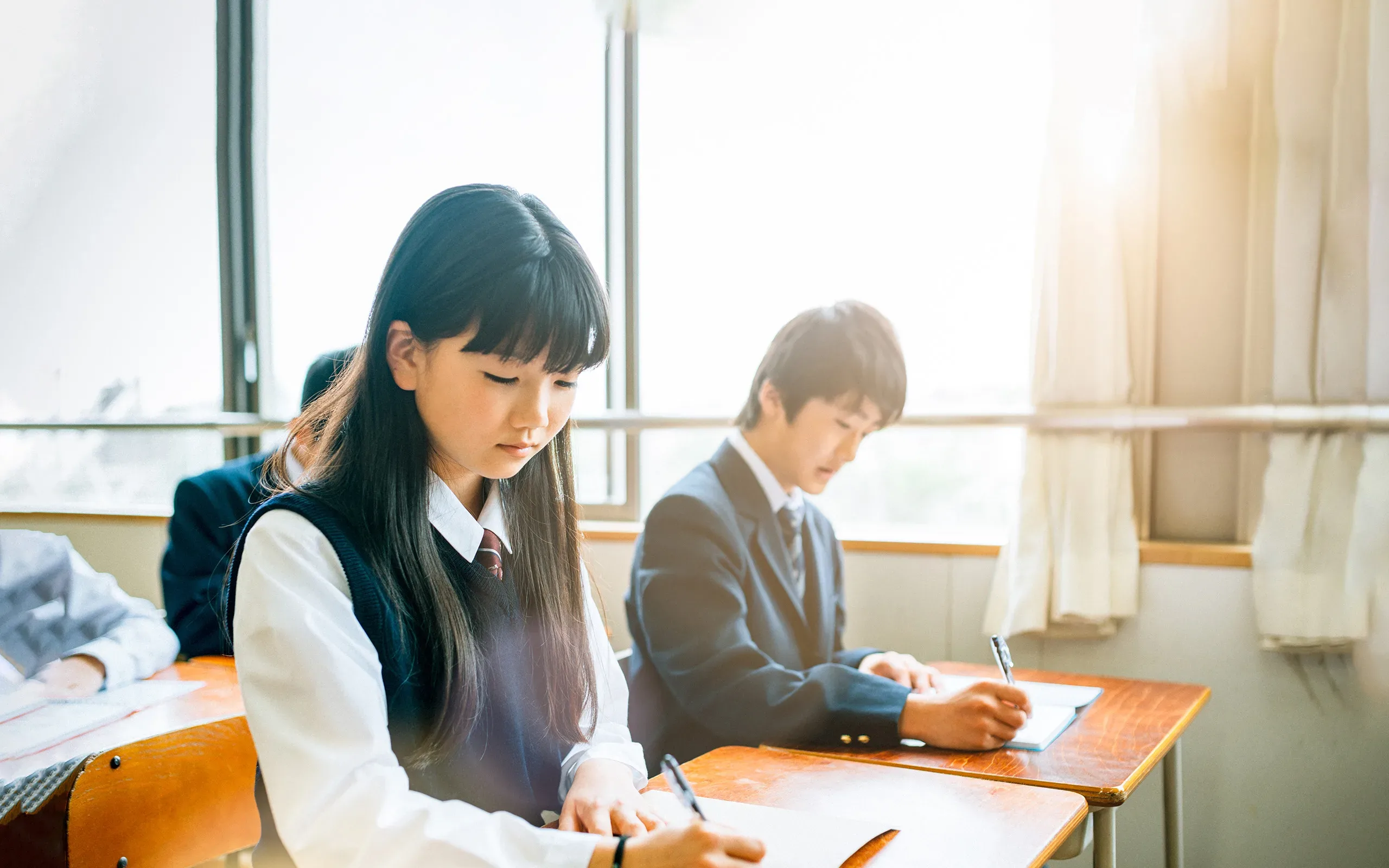 Photo d'un jeune fille japonaise, dans une classe, en train d'écrire sur un papier.