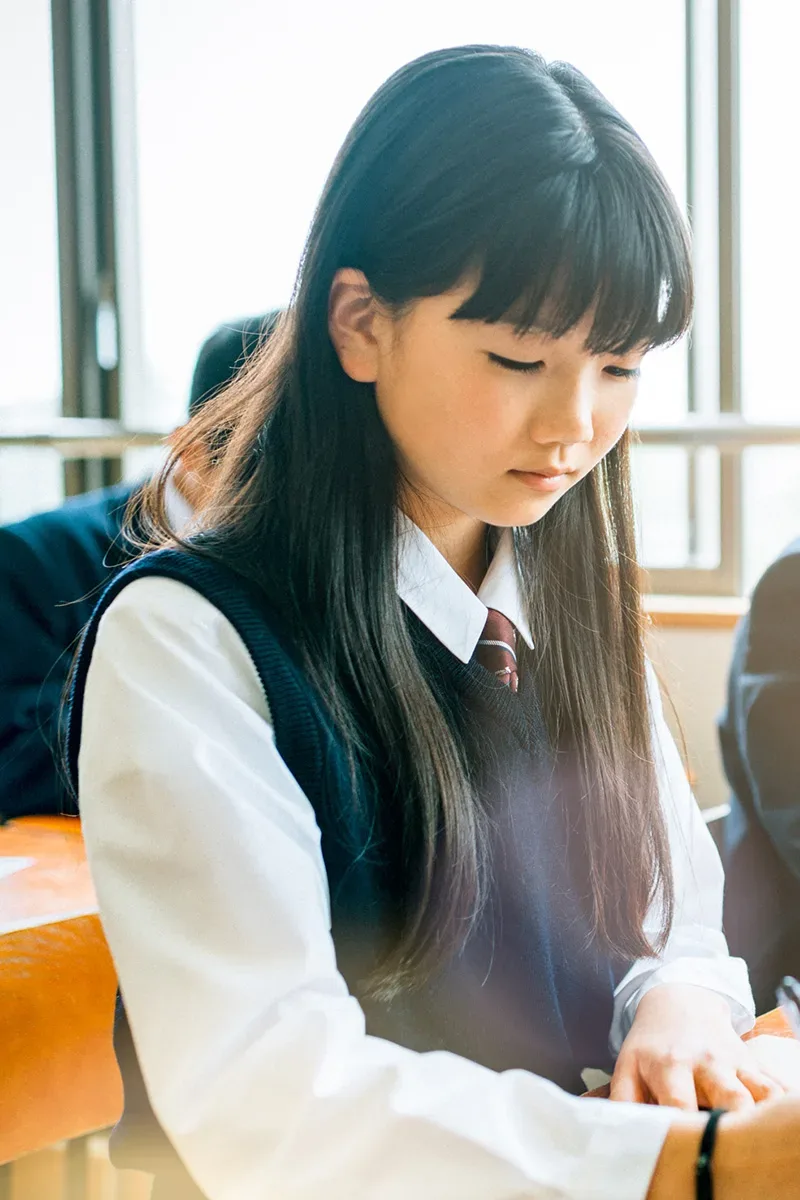 Photo d'un jeune fille japonaise, dans une classe, en train d'écrire sur un papier.