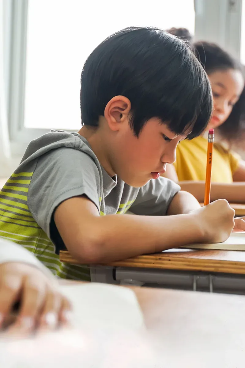Photo d'un jeune enfant japonais, dans une classe, en train d'écrire sur un papier.